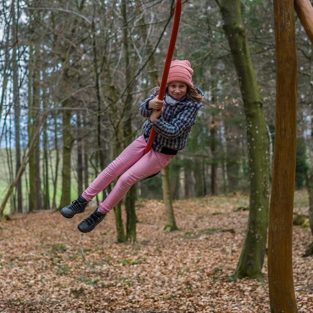 Kind hängt auf einer Tellerschaukel im Wald